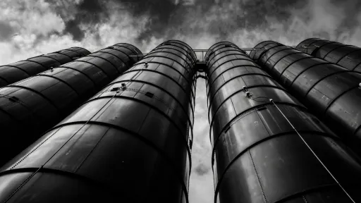 Dramatic upward view of industrial cylindrical silos against a cloudy sky in black and white