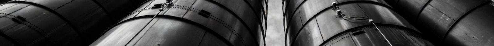 Dramatic low-angle view of industrial silos towering against cloudy sky in black and white
