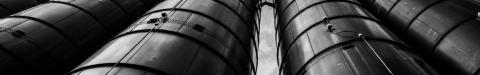 Dramatic low-angle view of industrial silos towering against cloudy sky in black and white