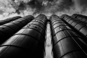 Dramatic low-angle view of industrial silos towering against cloudy sky in black and white